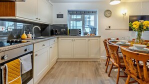 A modern kitchen with white cabinets, a stove, and a dining area with wooden chairs and a table. - 4 Bed in Bideford (oc-46840) (Pusehill)