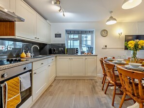 A modern kitchen with white cabinets, a stove, and a dining area with wooden chairs and a table. - 4 Bed in Bideford (oc-46840) (Pusehill)