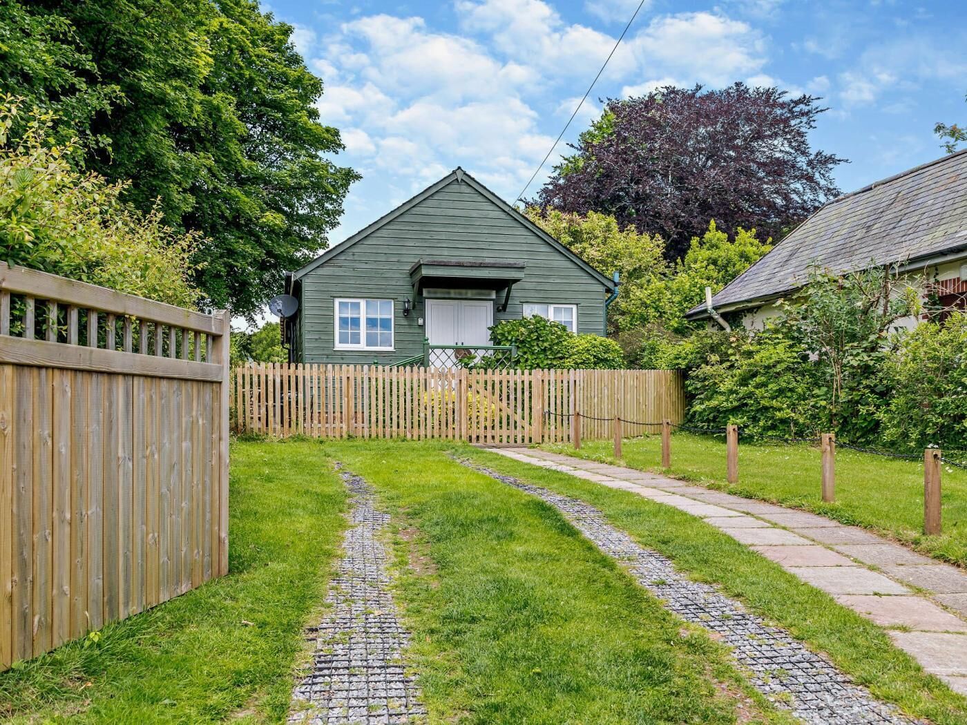 A green house with a paved driveway and a wooden fence.
