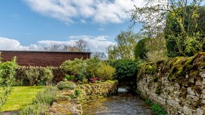 Un ponte di pietra sopra un ruscello, circondato da vegetazione lussureggiante e un edificio in legno.
