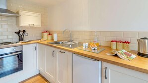Una cucina moderna con pensili bianchi, piano cottura in acciaio inossidabile, un lavello a due vasche e un bollitore.