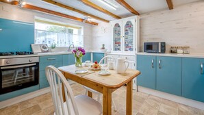 Een keuken met blauwgroene kastjes, een houten tafel en een raam met uitzicht.