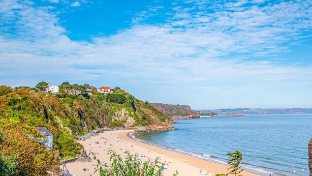 Ein Küstenstrand mit Gebäuden an einem Hügel, klarem Himmel und ruhiger See.
