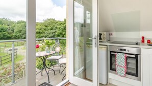 Ein Balkon mit Tisch und Stühlen, eine Küche mit Backofen und Mikrowelle sowie eine Glastür, die in einen Garten führt.