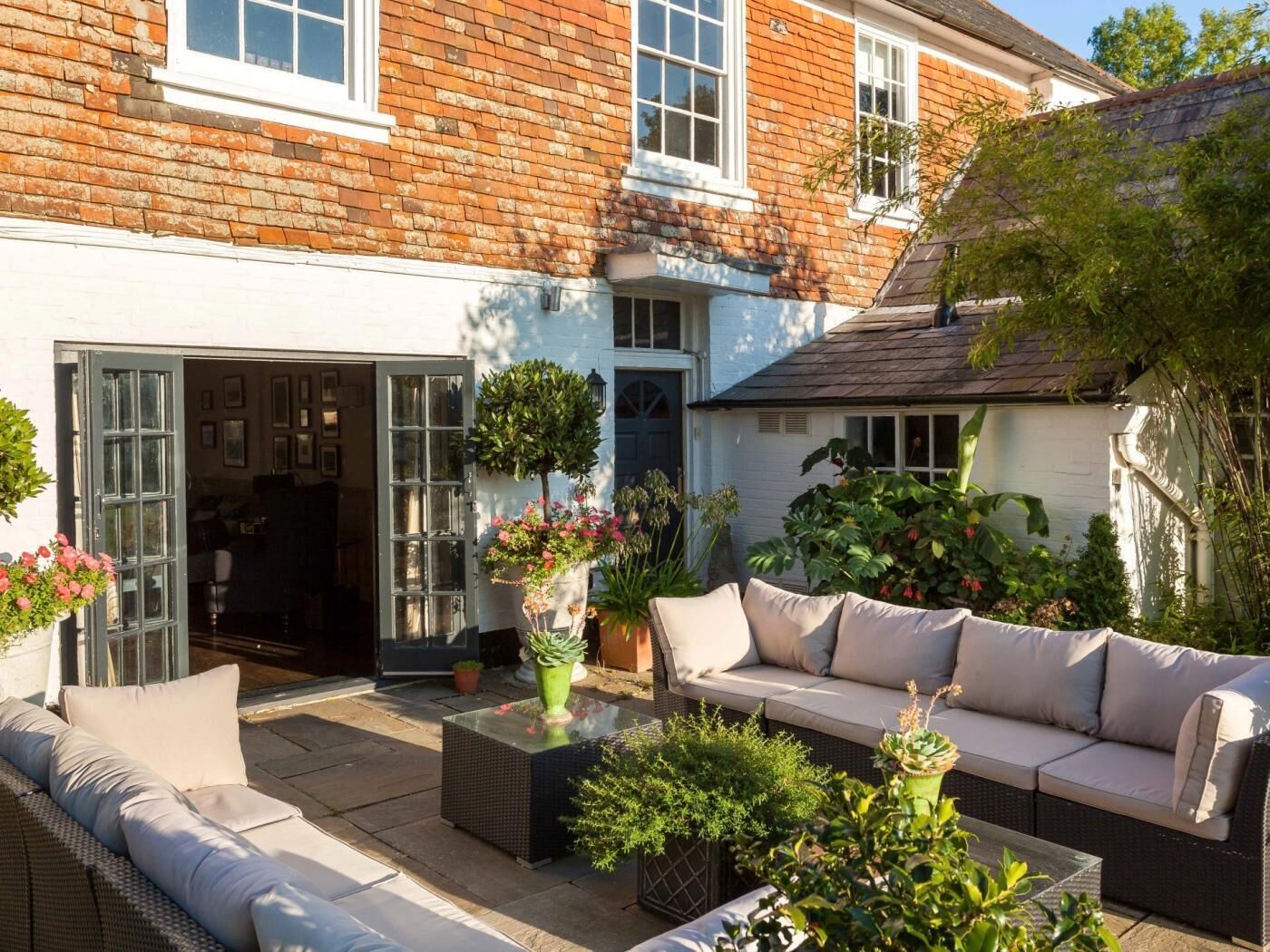 A cozy outdoor seating area with a sofa and chairs, surrounded by potted plants and a building with a brick facade.