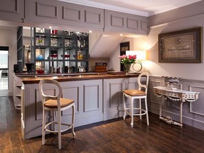 A bar area with a wooden counter, two bar stools, and a decorative table with a vase of flowers. - 5 Bed in Hurst Green (oc-46916) (Robertsbridge)
