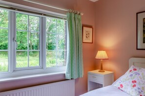 A bedroom with a window, a bedside lamp, a bed with floral pillows, and a framed picture on the wall.