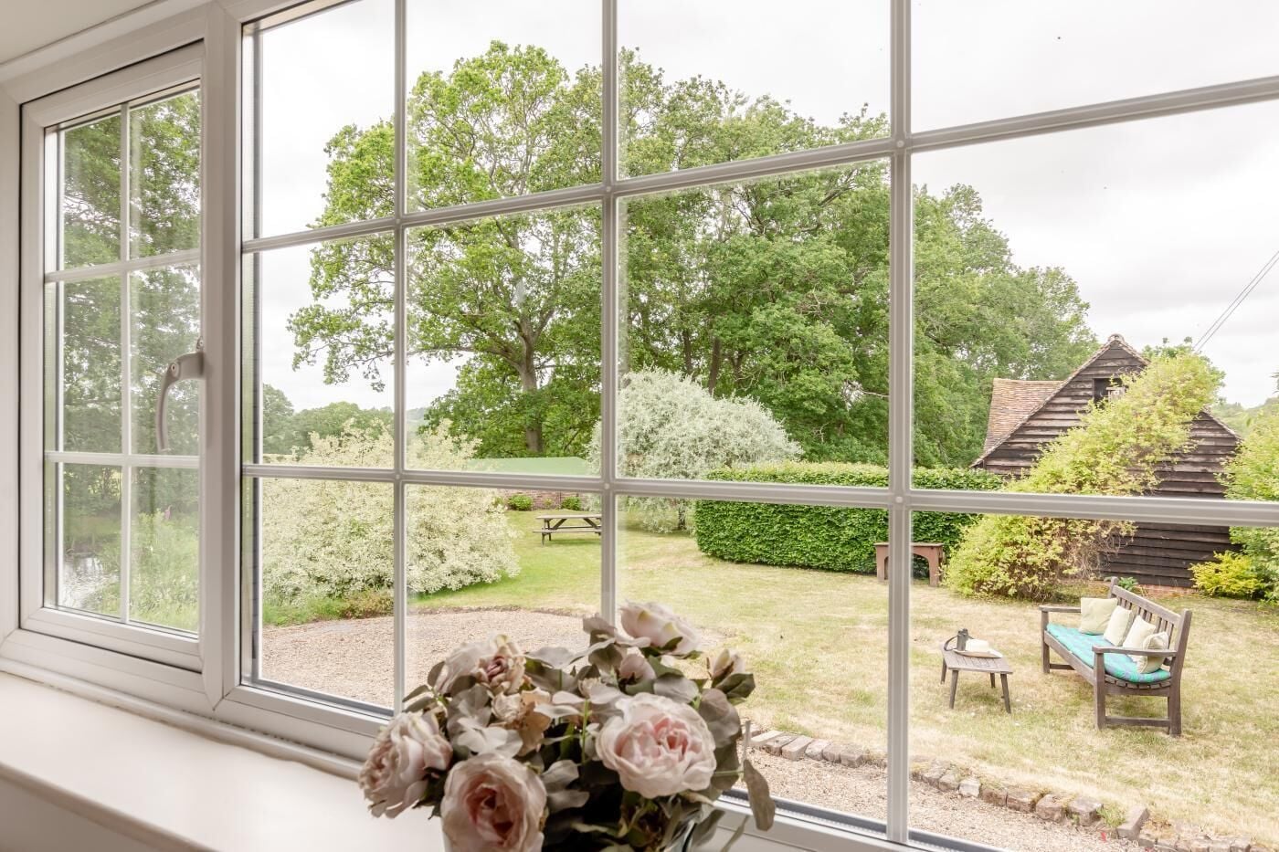 Ein Zimmer mit einem großen Fenster, das einen Blick auf einen Garten mit einer Holzkonstruktion, einer Bank und einem Picknicktisch bietet.