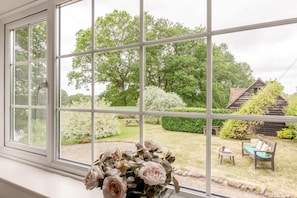 A room with a large window offering a view of a garden with a wooden structure, a bench, and a picnic table.