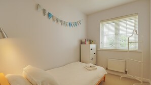 Ein Schlafzimmer mit einem Bett, einem Heizkörper, einem Fenster mit Jalousien, einem Kleiderschrank und einem an der Wand befestigten Regal mit Büchern.