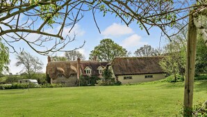 A traditional stone house with a thatched roof, a grassy lawn, and a clear sky. - 5 Bed in Sturminster Newton (oc-76458) (Woodrow)