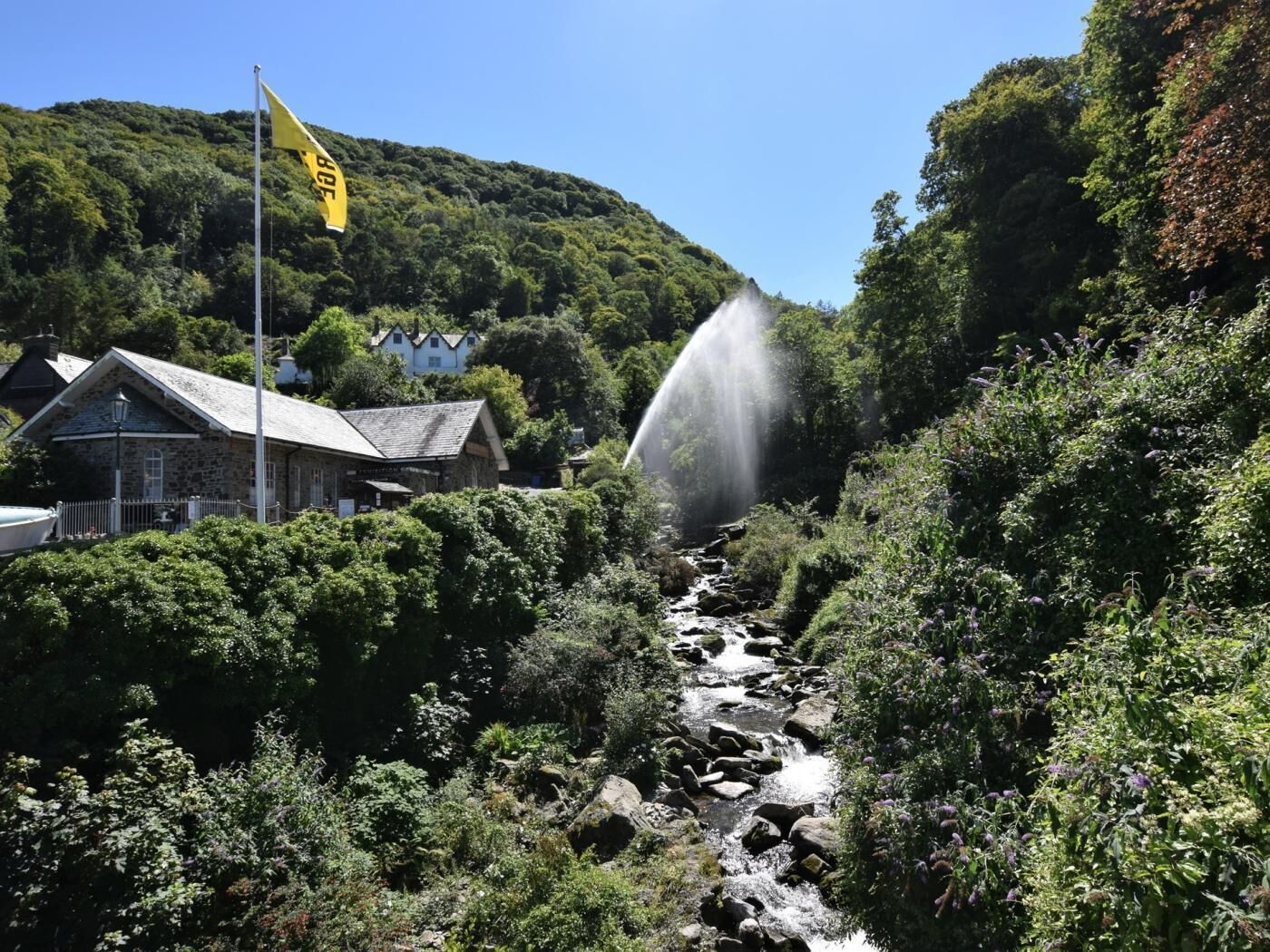 Um edifício de pedra com uma bandeira, uma cascata e vegetação exuberante.