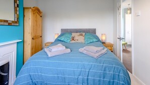 Quarto com uma cama, duas mesas de cabeceira, um criado-mudo, um guarda-roupa de madeira e um espelho na parede.