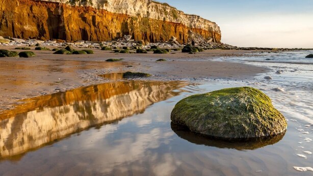 A coastal landscape with a sandy beach, a large rock in the foreground, and a cliff with layered rock formations. - 3 Bed in Hunstanton (oc-78821) (Hunstanton)