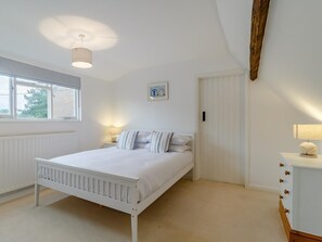 A bedroom with a white bed, a bedside table with a lamp, a radiator, a window, and a door. - 3 Bed in Hunstanton (oc-78821) (Hunstanton)