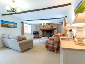 A living room with a sofa, a plaid chair, a fireplace, and a television. - 3 Bed in Hunstanton (oc-78821) (Hunstanton)