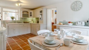 A kitchen with white cabinets, a dining table set with white dishes, and a clock on the wall. - 3 Bed in Hunstanton (oc-78821) (Hunstanton)