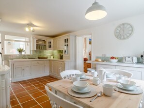 A kitchen with white cabinets, a dining table set with white dishes, and a clock on the wall. - 3 Bed in Hunstanton (oc-78821) (Hunstanton)
