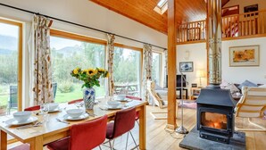 A dining area with a table set for four, a vase of sunflowers, and a wood-burning stove. - 4 Bed in Fort William (oc-78875) (Muirshearlich)