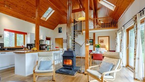 A spacious living area with a fireplace, wooden ceiling beams, and a kitchen in the background. - 4 Bed in Fort William (oc-78875) (Muirshearlich)