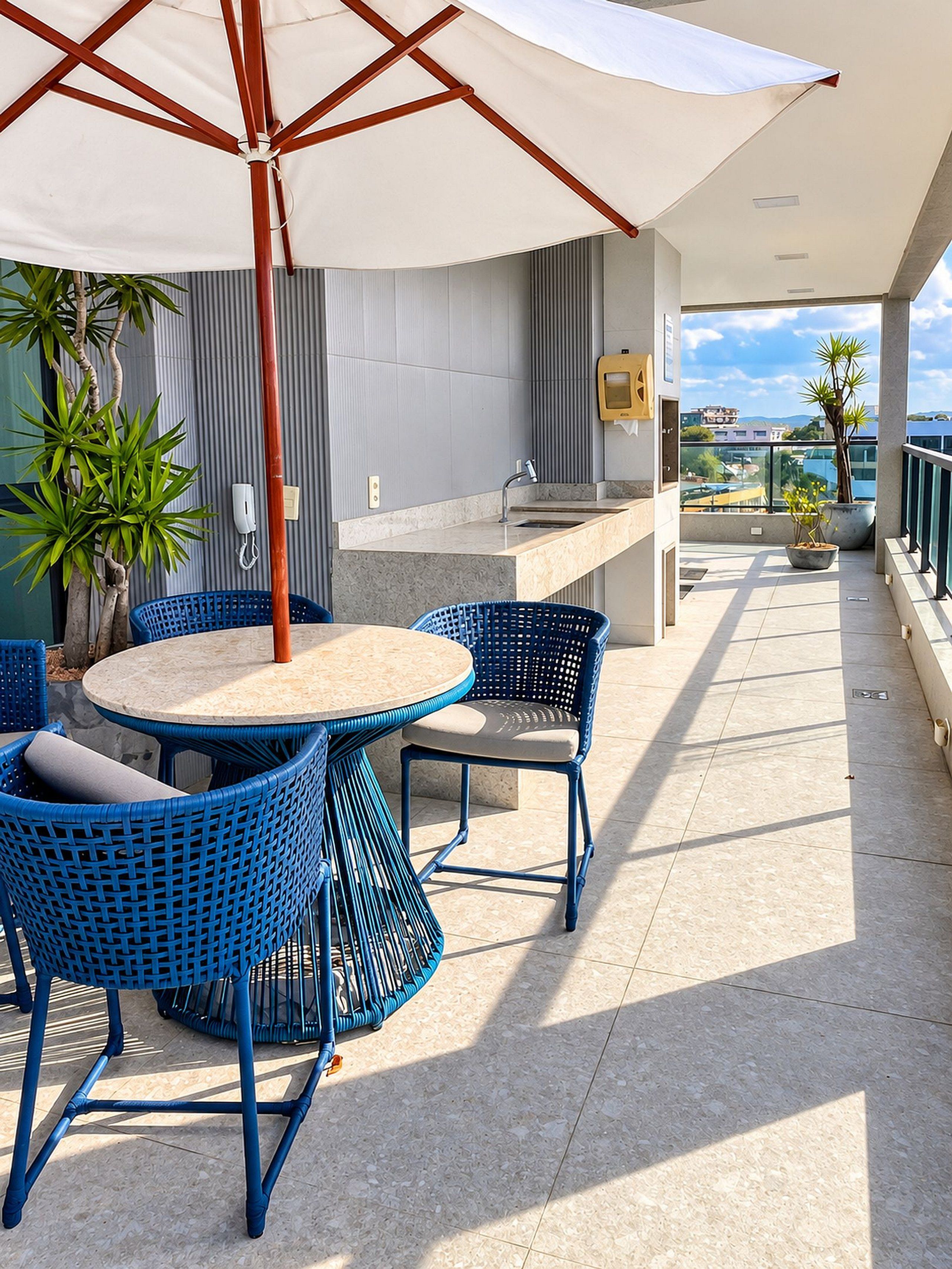 Una terraza con una mesa redonda y sillas azules, un paraguas blanco y vistas de la ciudad.