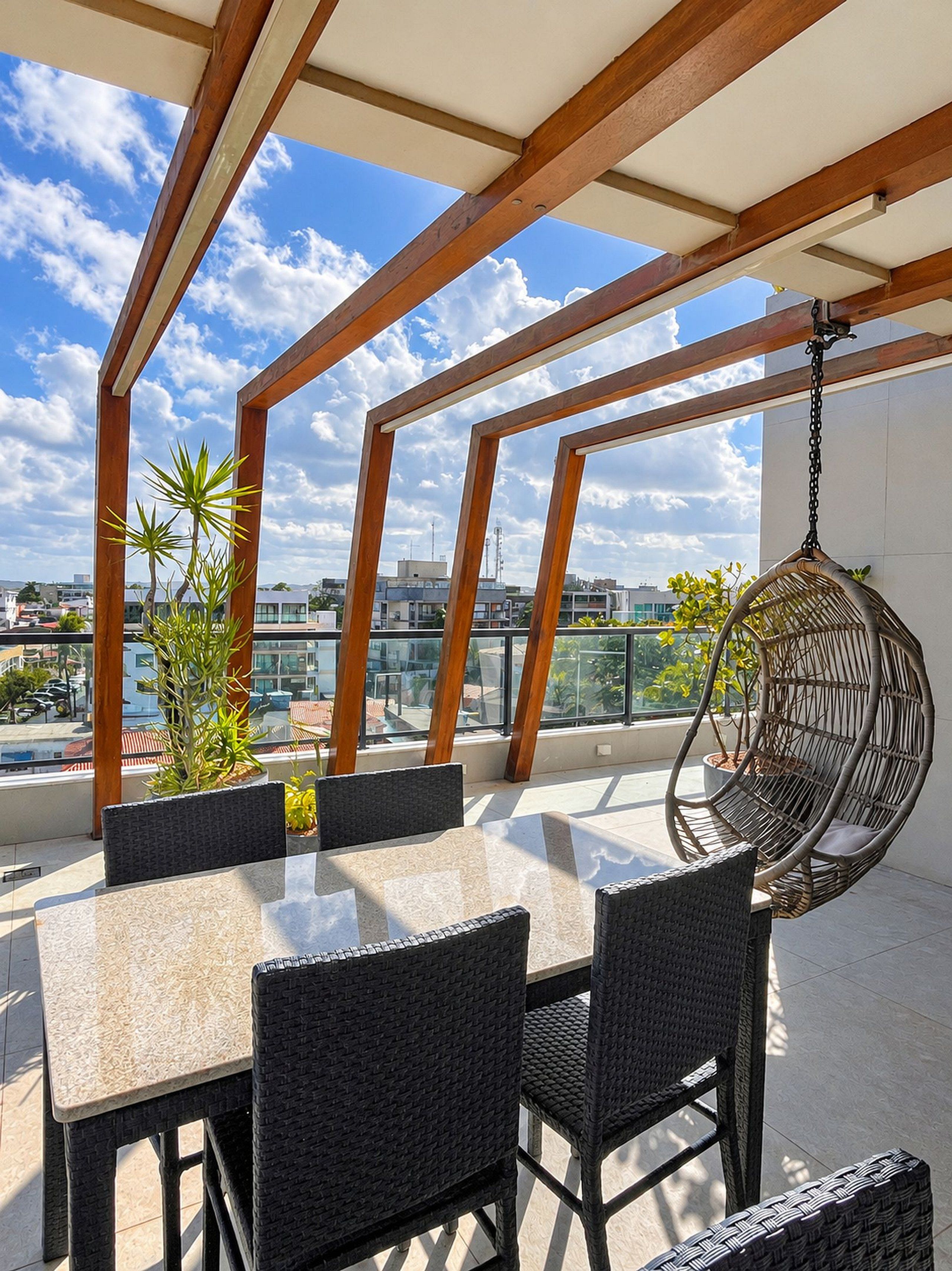 Una terraza al aire libre con una mesa, sillas, una hamaca colgante y plantas en macetas.