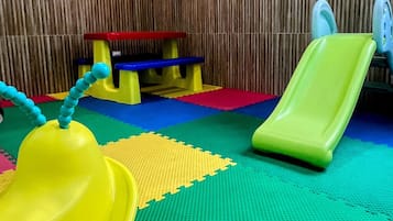 Zona de juegos con un tobogán, una banca y una mesita.