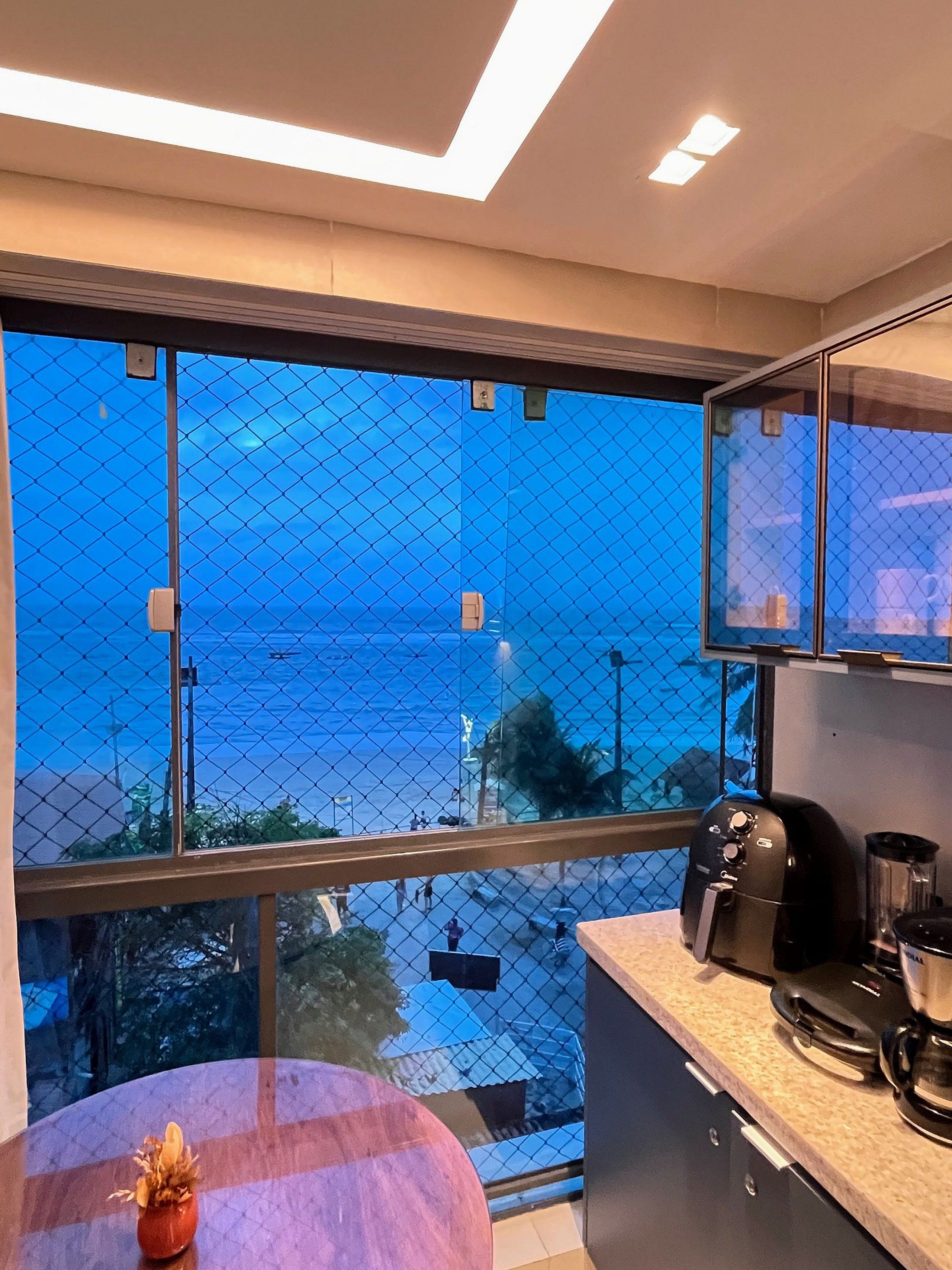 Een balkon met uitzicht op zee, een koffiezetapparaat en een blender op het aanrecht.