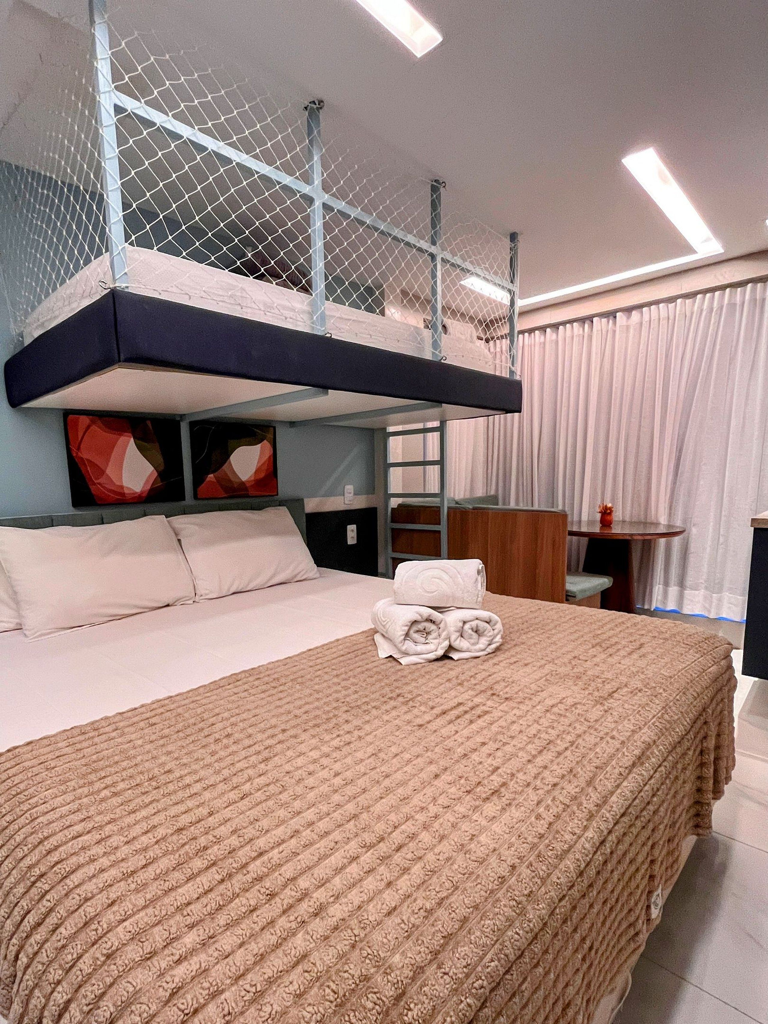 Hotelkamer met een stapelbed, een bureau, een stoel, een klein tafeltje en een bed met een geruite deken.