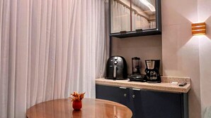 Moderni hotellihuone, jossa on pyöreä pöytä, kahvinkeitin ja peili tummanvärisen kaapin yläpuolella.