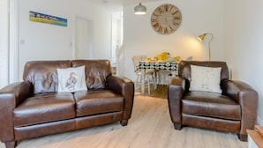 Ein Wohnzimmer mit zwei Ledersofas, einem Esstisch mit Stühlen, einer großen Wanduhr und einem Gemälde an der Wand.