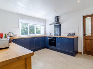 A modern kitchen with dark blue cabinets, a wooden countertop, a built-in oven, and a window providing natural light. - 3 Bed in King's Lynn (oc-78973) (Syderstone)