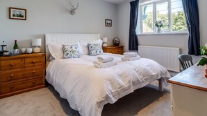 Une chambre à coucher comprenant un lit, une commode en bois, des tables de chevet, une fenêtre avec des rideaux et une décoration murale représentant une tête de cerf.