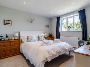 A bedroom with a bed, wooden dresser, bedside tables, a window with curtains, and a wall-mounted deer head decoration. - 3 Bed in King's Lynn (oc-78973) (Syderstone)