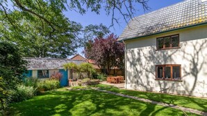 Un jardin bien entretenu, avec une pelouse, une table et des chaises en bois, et un bâtiment blanc doté de fenêtres.