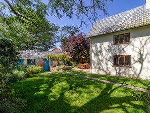 A well-maintained garden with a lawn, a wooden table and chairs, and a white building with windows. - 3 Bed in King's Lynn (oc-78973) (Syderstone)