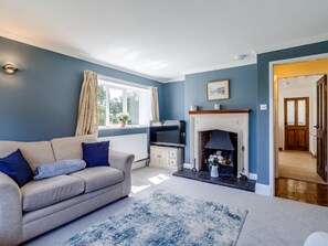 A living room with a sofa, a fireplace, a television, and a window with curtains. - 3 Bed in King's Lynn (oc-78973) (Syderstone)