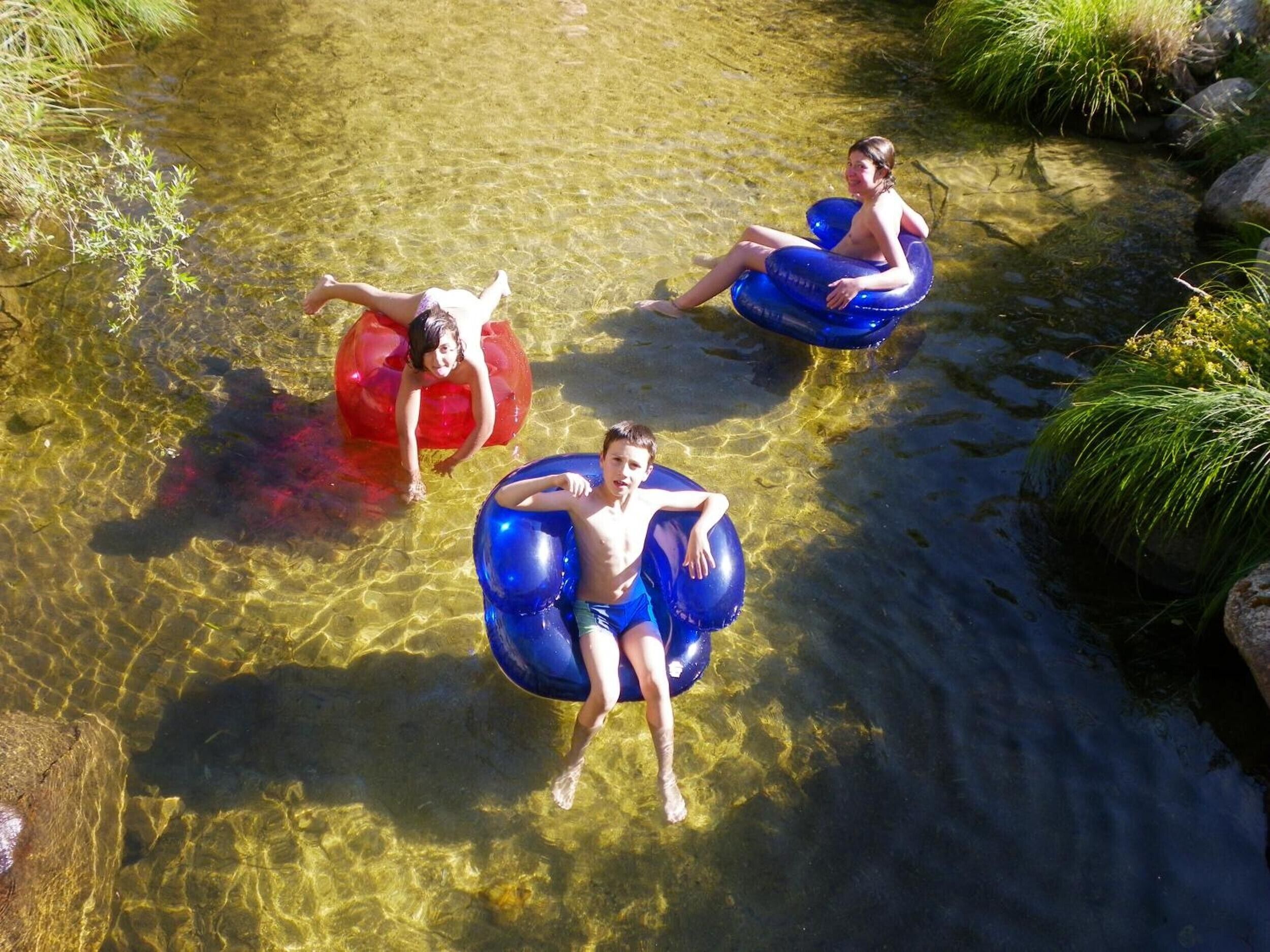 Three people floating in clear water using inflatable tubes.