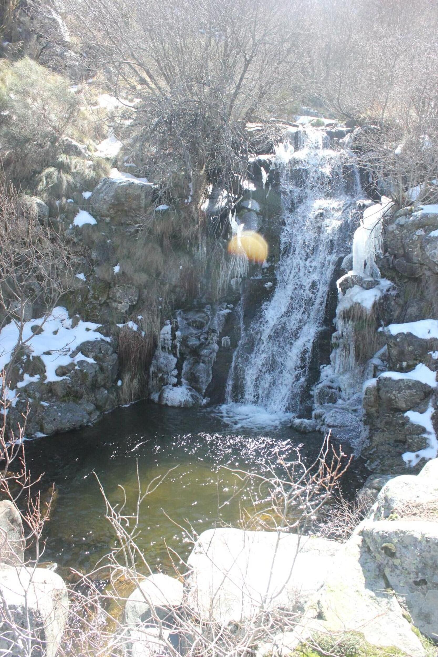 A waterfall surrounded by rocks and sparse vegetation.