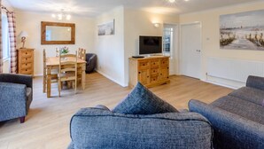 A living room with a sofa, a TV, a wooden cabinet, and a dining area with a table and chairs. - 3 Bed in Freshwater (oc-79039) (Freshwater)