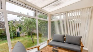 A conservatory with a sofa and chair, a small table, and a view of a garden. - 3 Bed in Freshwater (oc-79039) (Freshwater)