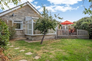 A stone house with a fenced backyard, a small tree, and a red umbrella.