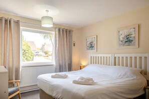 Een slaapkamer met een groot bed, een raam met gordijnen, een radiator, een nachtkastje en twee aan de muur hangende schilderijen.