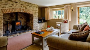 Ein gemütliches Wohnzimmer mit Kamin aus Stein, einer Couch, einem Tisch mit Büchern und einem Fenster mit Vorhängen.