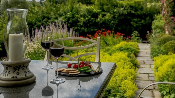 Ein Tisch im Freien mit Kerze, Weingläsern und einer Käseplatte mit Tomaten und Crackern.