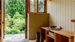 Eine hölzerne Bank mit Stiefeln und einem Korb, ein Fenster mit Blick ins Grüne und eine Tür, die nach draußen führt.