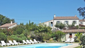 A pool with lounge chairs, a large house with a tiled roof, and surrounding greenery.