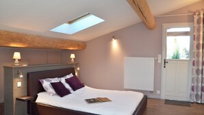 A bedroom with a skylight, a bed with pillows, bedside lamps, a radiator, and a door with curtains.