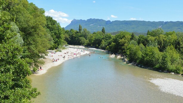 A river surrounded by dense greenery and mountains in the background.