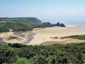 Paisagem costeira com uma praia arenosa, colinas verdes e céu limpo.